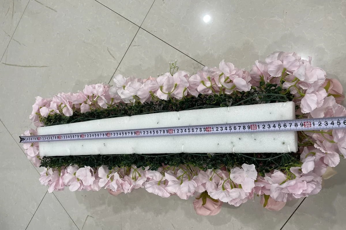 Back of an artificial flower table runner showing the foam base and green backing with a tape measure